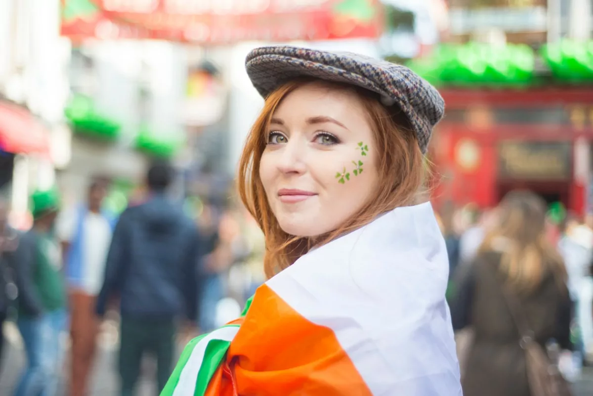 Irlandesa em close, no meio da rua, com trevo de três folhas pintado no rosto