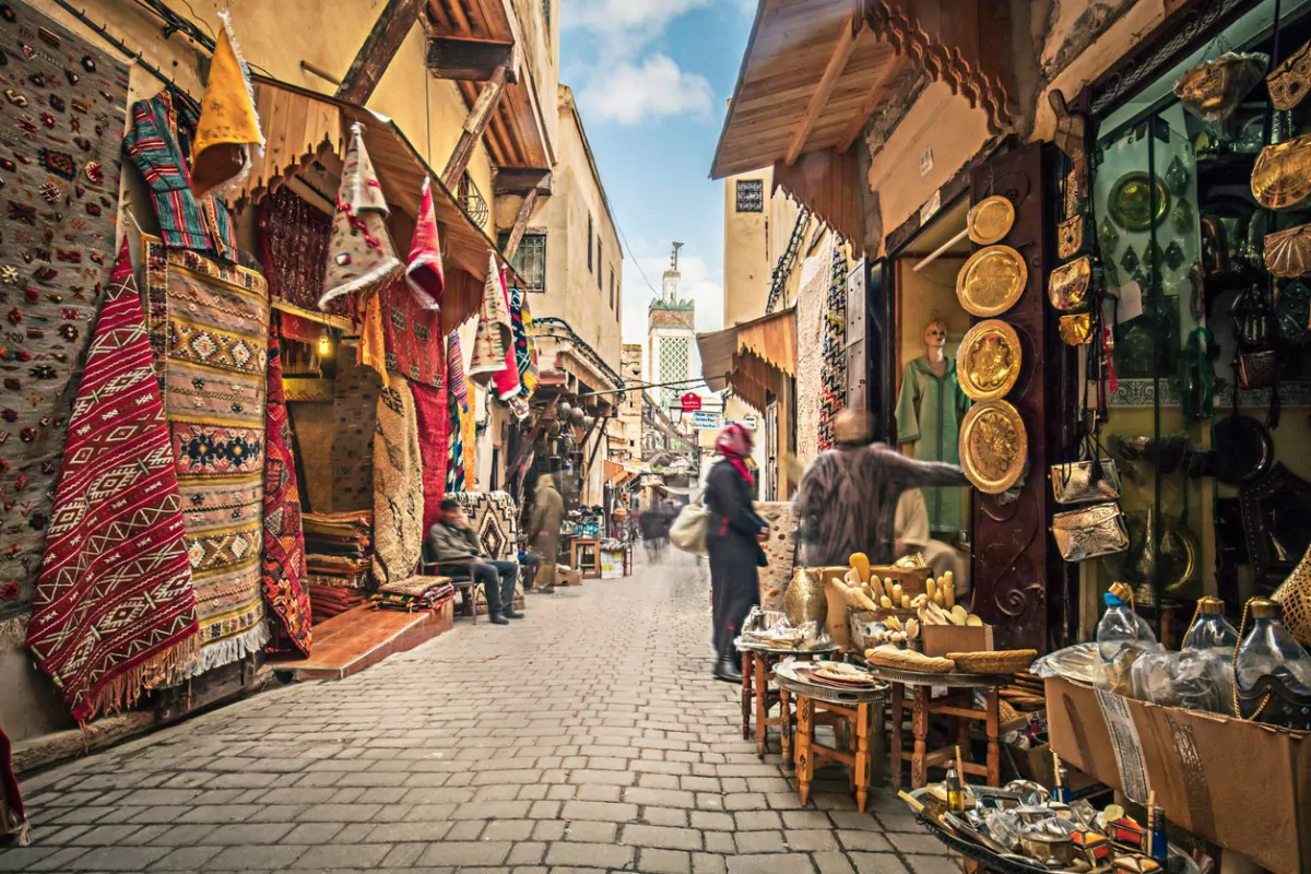 Ruas colorida de fez, em Marrocos, com tapetes e outros produtos pendurados e pessoas passeando