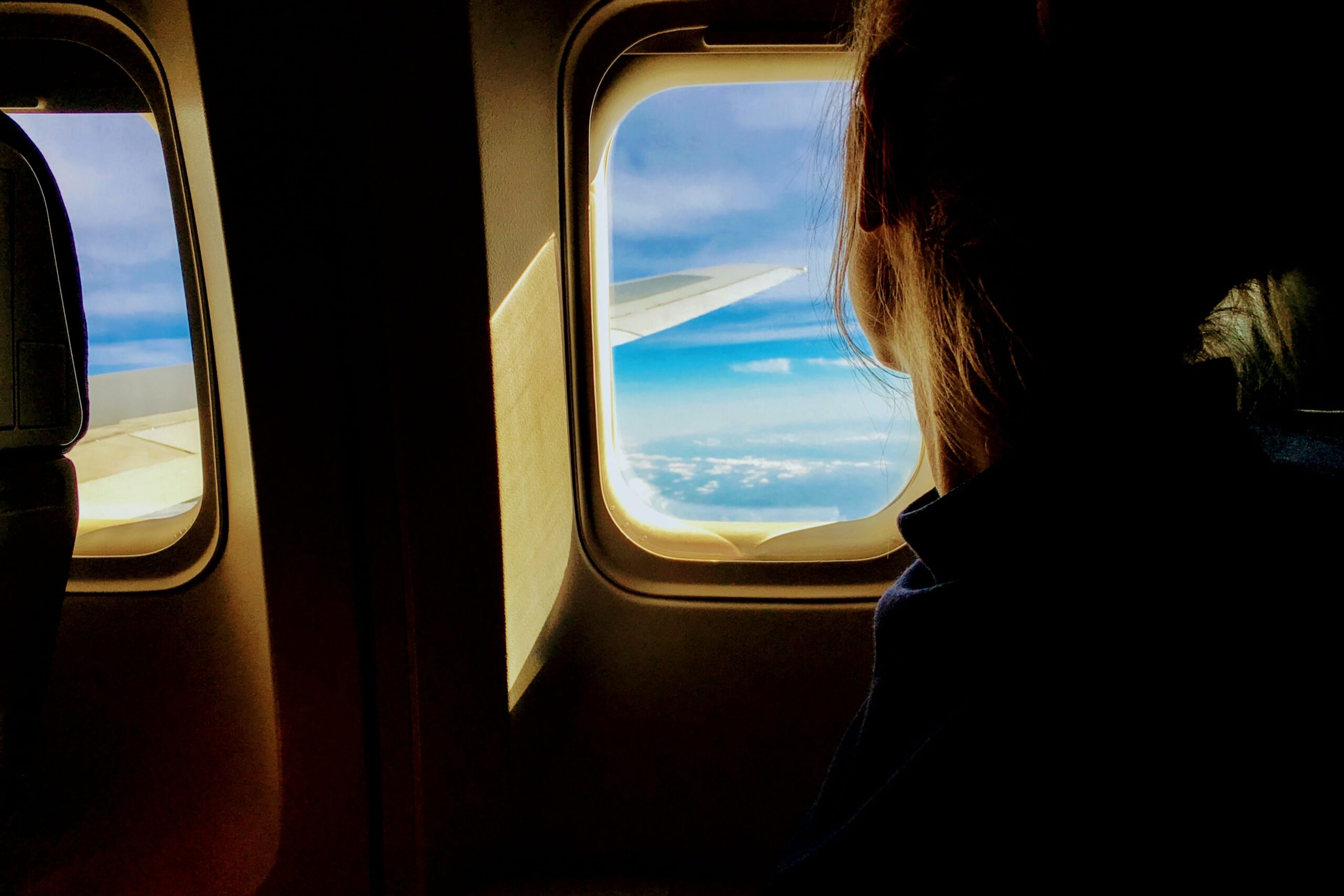 Viagens na pandemia: garota sentada no avião observa o céu pela janela quadrada.