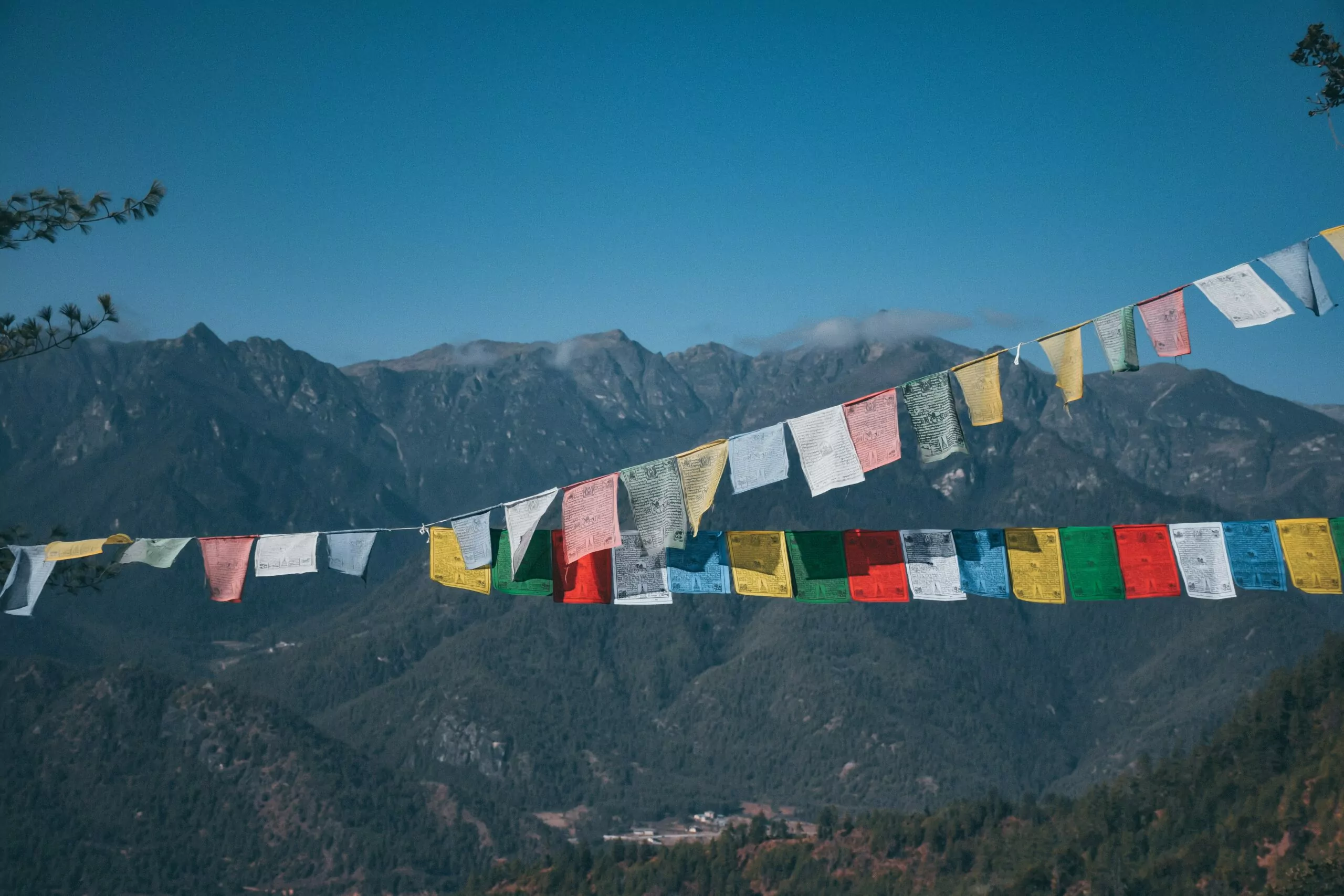 Bandeirinhas coloridas pendurada em um varal. Ao fundo, a Cordilheira do Himalaia, com montanha coberta de neve contrastando com céu azul. Carbono negativo.