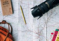 Planejar uma viagem: mapa, câmera fotográfica, mochila e cadernos estão sobre uma mesa.