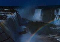 Cataratas do Iguaçu durante a noite, com um arco-íris se formando na paisagem das quedas d'água.