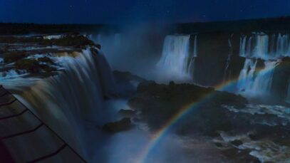 Cataratas do Iguaçu durante a noite, com um arco-íris se formando na paisagem das quedas d'água.