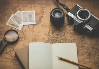 Viajar em segurança. Imagem mostra mapa aberta com caderno de anotações, máquina fotográfica e lupa.