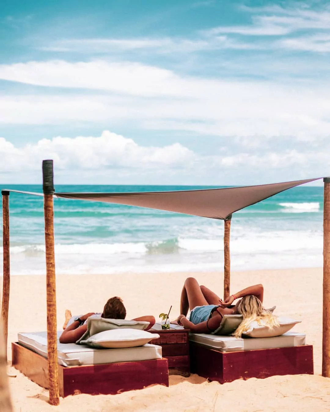 Casal deitado em cadeiras cobertas por uma tenda na praia da Península de Maraú.