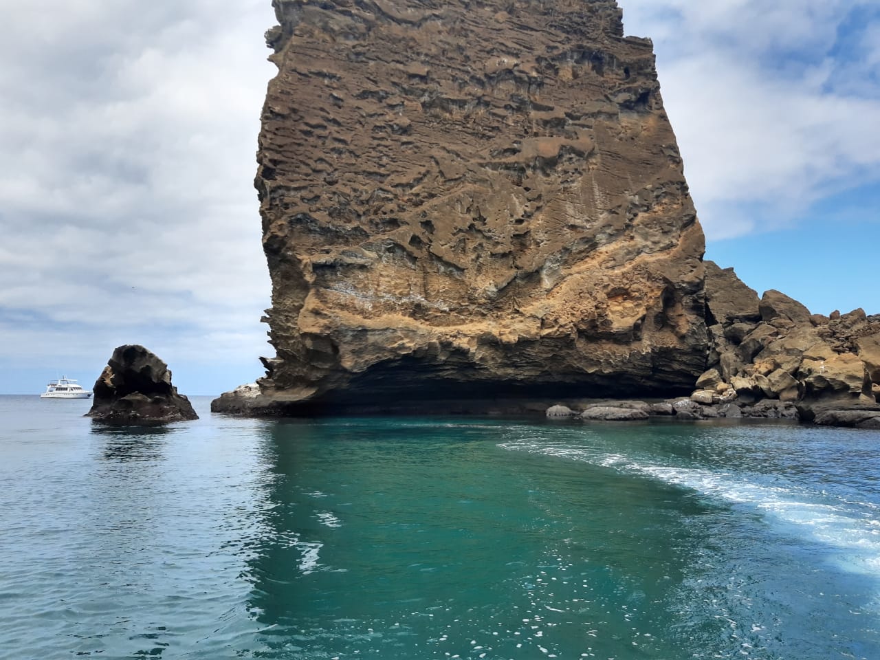 O que mudou nas viagens. Foto do mar azul esverdeado, com uma grande pedra em formato oval formando uma parede no meio.