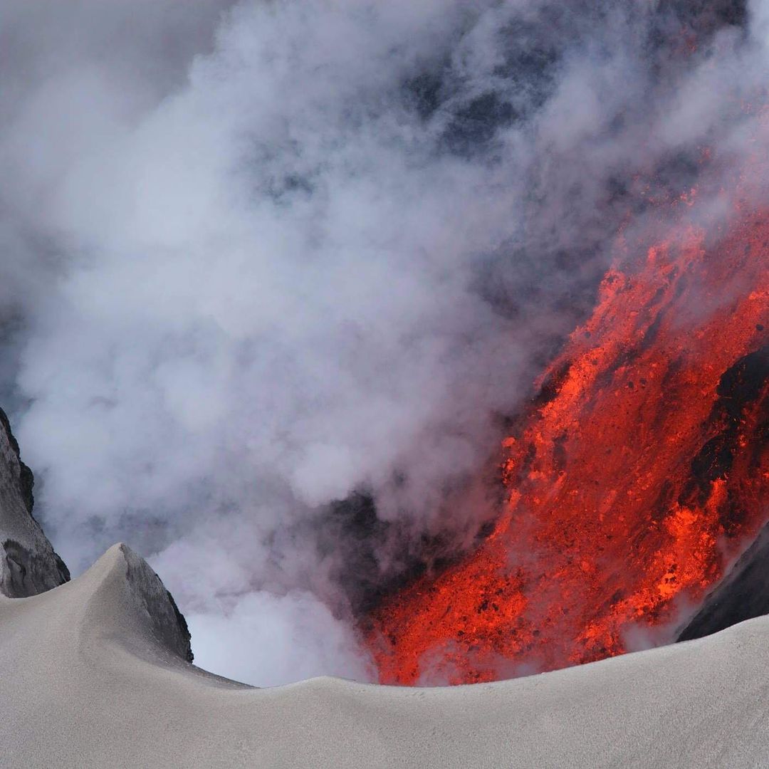 A imagem foca na lava de um vulcão, avermelhada e rodeada por fumaça. Viajar para a Islândia.