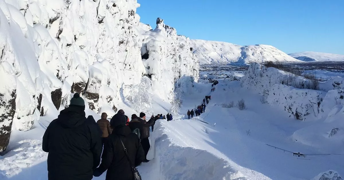Em cenário de neve, algumas pessoas caminham de costas para a imagem e descobrem como é a Islândia.