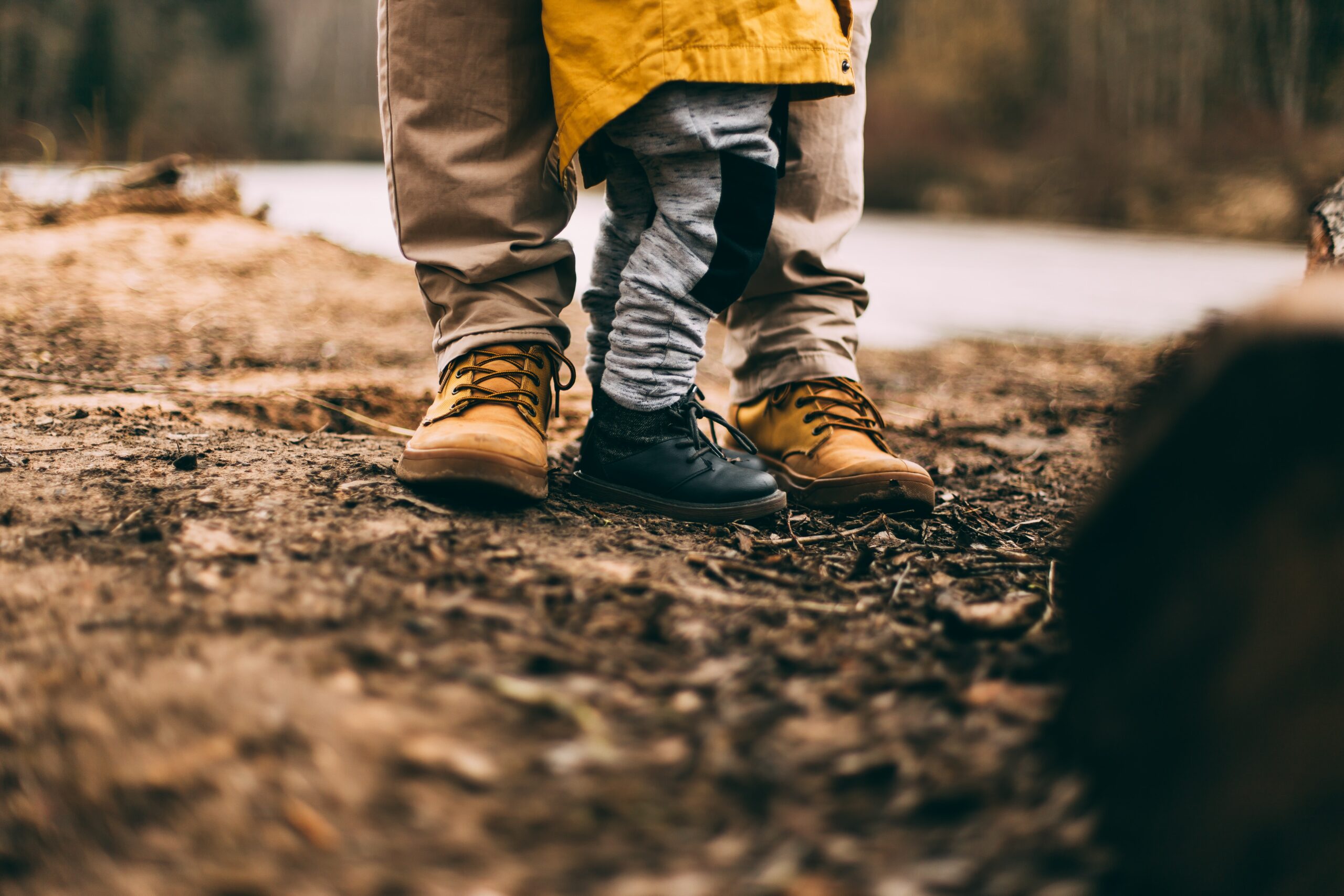 detalhe dos pés de pessoa adulta com criança ao lado, ambos trajados e calçados para caminhada ou trilha