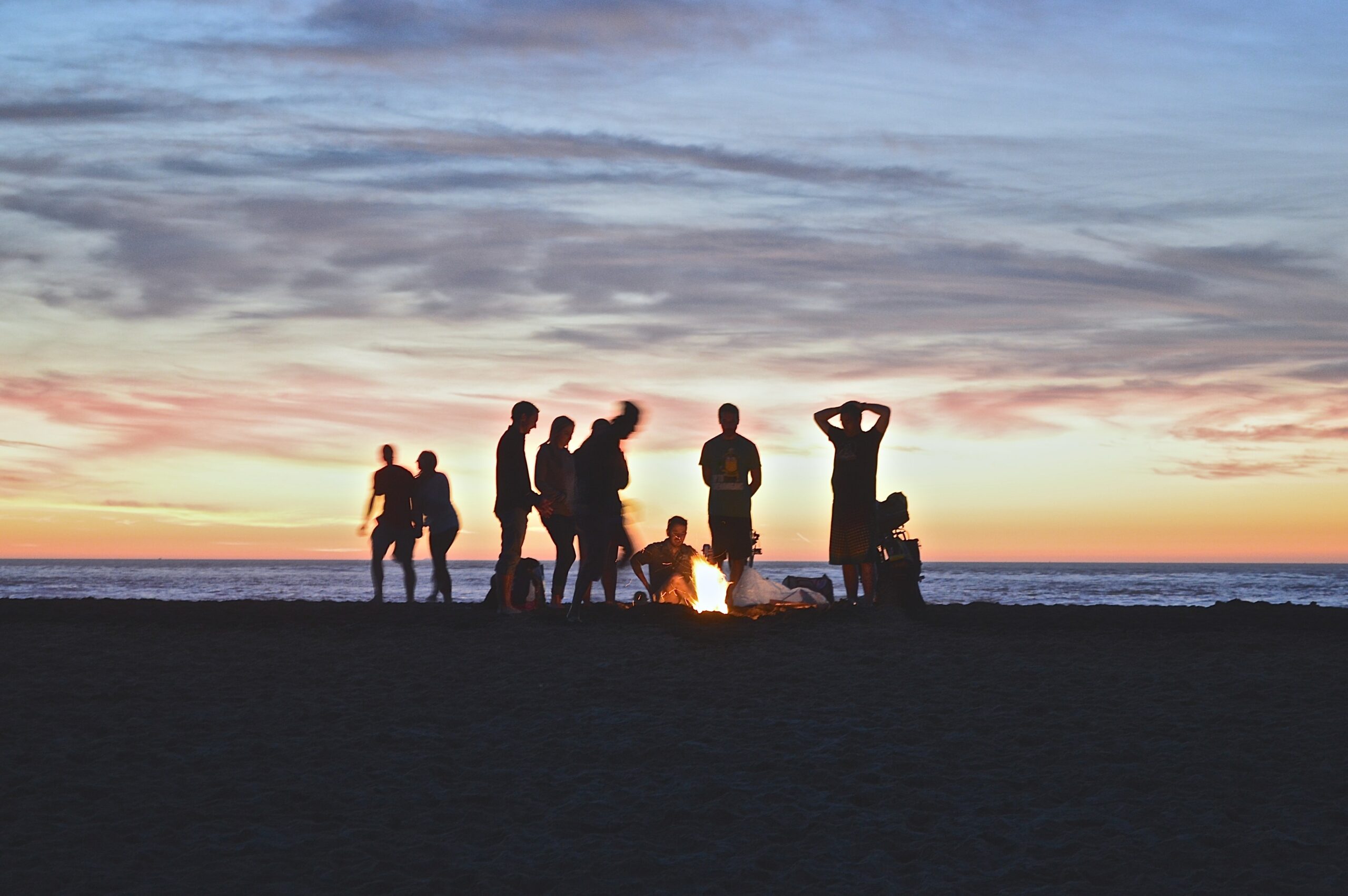 grupo de viajantes à beira de fogueira na praia ao por do sol