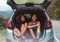 moças no porta malas aberto de um carro em viagem por estrada