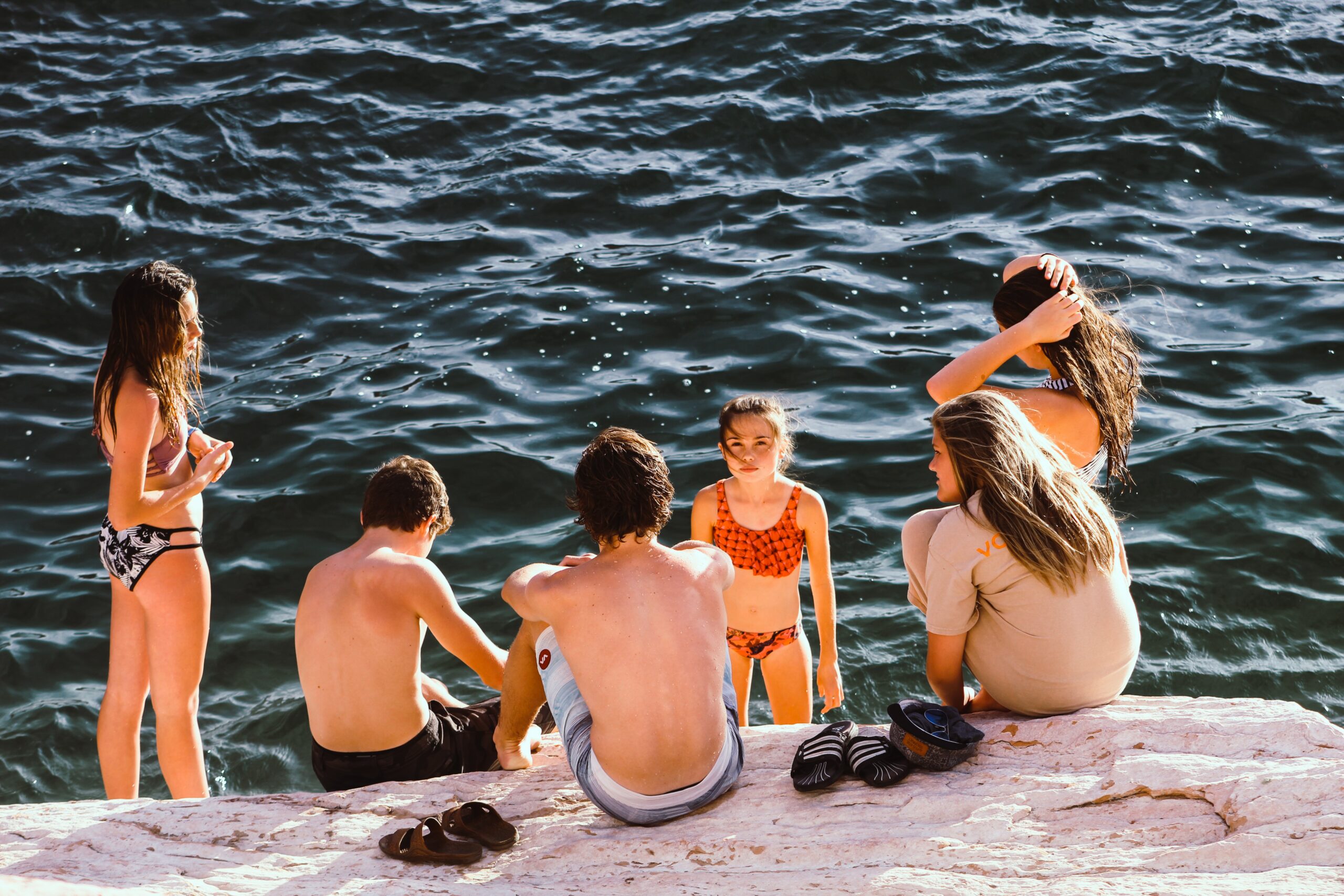 uma família em trajes de banho, crianças e adultos, sentados em uma pedra à beira mar