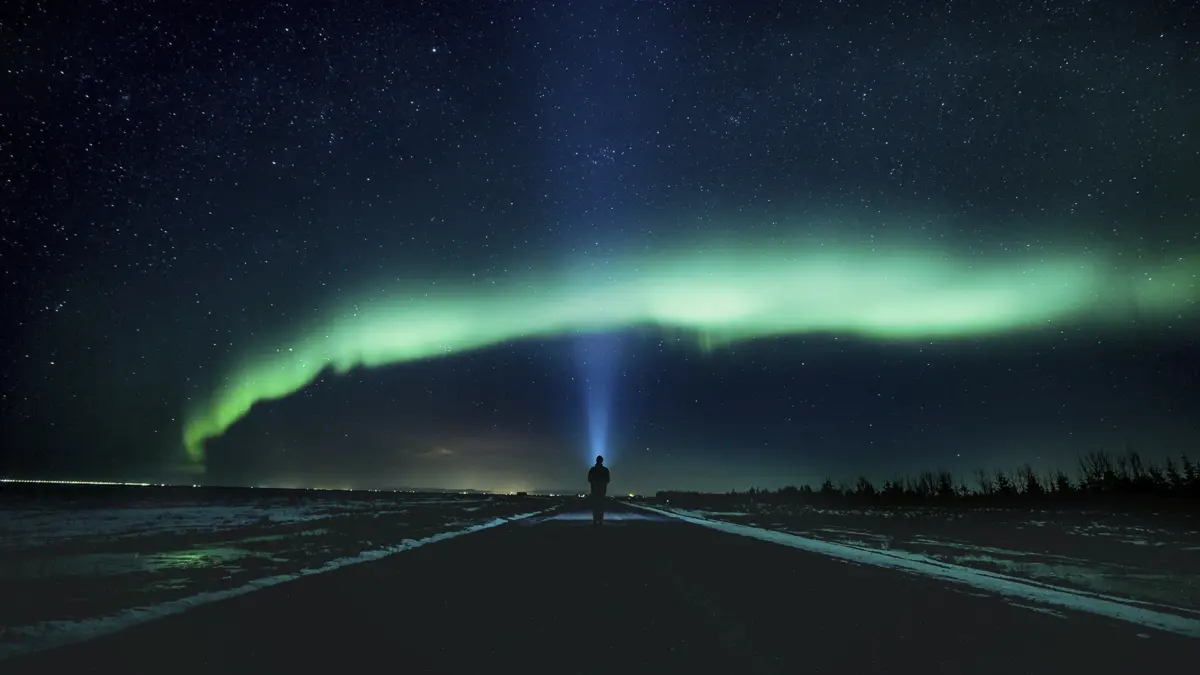 islandia-4 Imagem de uma pessoa com uma lanterna observando a aurora boreal.