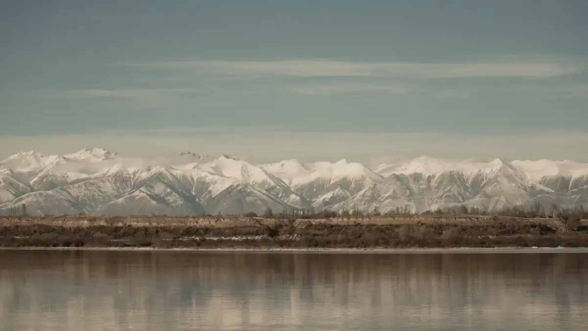 quirguistao-lago-issyk-kul Imagem do Lago Issyk-Kul com montanhas nevadas ao fundo.