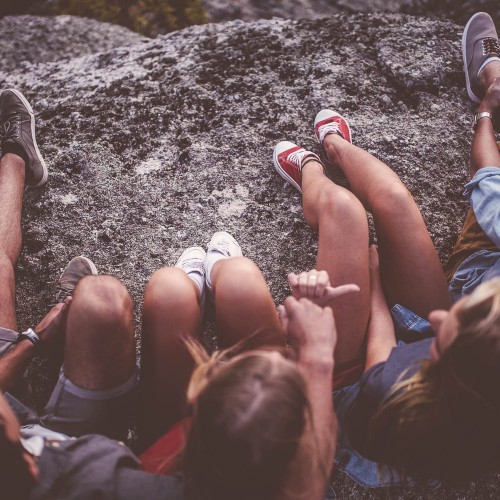 Cropped image of the legs and footwear of teenagers sitting on rocks together outdoors