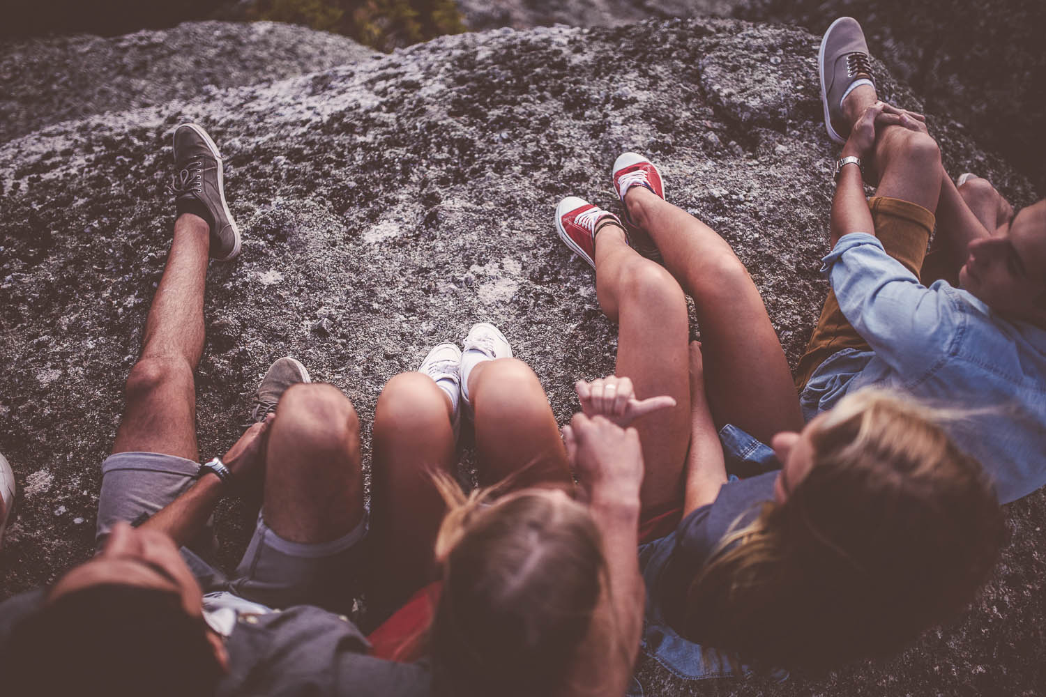 Cropped image of the legs and footwear of teenagers sitting on rocks together outdoors